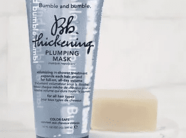 A tube of bumble and bumble thickening plumping mask displayed upright on a marble surface, with a blurred background emphasizing the product’s details.