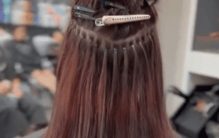 Back view of a person's head at a hair salon, showing long brown hair sectioned with several clips for styling, in a professional setting.