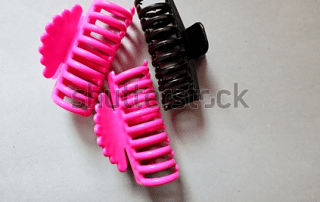 Two colorful hair claw clips, one pink and one black, are lying on a light grey surface, positioned in an overlapping manner.