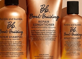 Three bumble and bumble bond-building hair care products on a peach background: repair shampoo, conditioner, and repair treatment, all labeled as color safe.