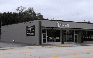 Exterior view of a modern one-story commercial building housing "j. bauman salon" and "florida fitness," featuring a flat façade with large windows and dedicated parking in front.