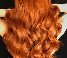 A woman with vibrant copper-colored hair, displaying long, luxurious curls against a dark background.