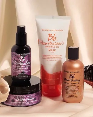 An arrangement of bumble and bumble hair care products, including sprays, masks, and treatments set against a soft beige backdrop with gentle light draping.