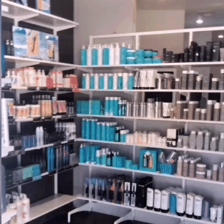 A neatly organized salon retail shelf displaying various hair care products including shampoos, conditioners, and styling products in a modern, brightly lit interior.