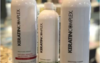 Three keratin complex hair product bottles on a counter, two large on the sides and one smaller in the middle, all with labels facing forward.