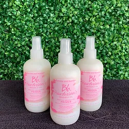 Three bottles of bumble and bumble hairdresser's invisible oil primer displayed against a lush green leafy background.