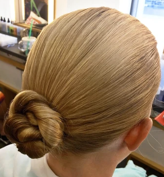 Back view of a person's neatly styled hair, featuring a smooth, sleek blonde bun at the nape of the neck in a salon setting.