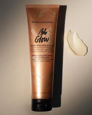 A tube of bumble and bumble "glow" bond-building styler on a neutral background with a dollop of the cream spilled next to it, highlighting the product's texture.