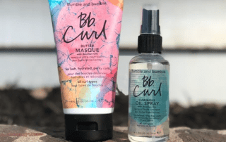 Two bumble and bumble curl hair products arranged outdoors. on the left, a colorful bb curl butter masque tube, and on the right, a transparent bb curl oil spray bottle.