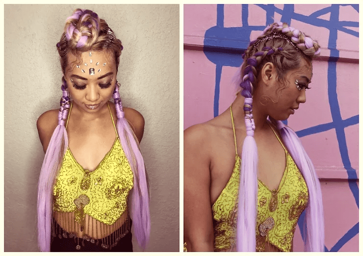 A woman with intricate purple braids and decorative face paint, wearing a yellow lace top, is shown in two poses: front and profile, against a pink and blue background.