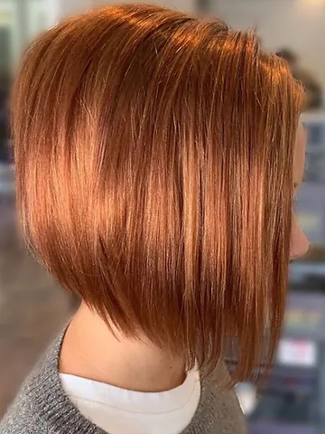 Side view of a woman with a shiny, copper-colored bob haircut. the hair is neatly styled with smooth texture and subtle highlights, reflecting a professional and chic appearance.