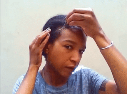 A woman with short hair applies product to her hair and scalp, massaging it in with her fingertips. she wears a blue t-shirt and a bracelet, looking focused on her hair care routine.