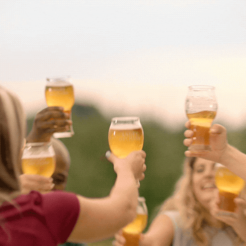 A cheerful group of friends toasting with glasses of beer outdoors, focusing on the glasses in a close-up shot, with a blurred natural background.