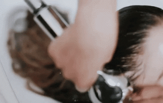 A woman getting her hair washed at a salon, with the shampoo being applied directly from the bottle onto her wet hair.