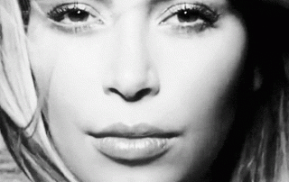 Black and white close-up image of a woman with tousled hair softly looking into the camera, showcasing striking facial features and intense eyes.