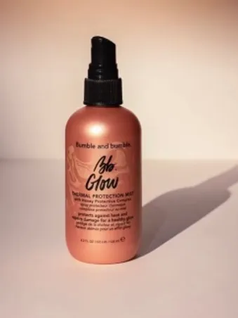 A spray bottle of bumble and bumble glow thermal protection mist displayed against a softly lit beige background.