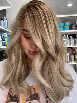 Woman with long wavy blonde hair with highlights, covering most of her face, showcasing the hairstyle in a salon.