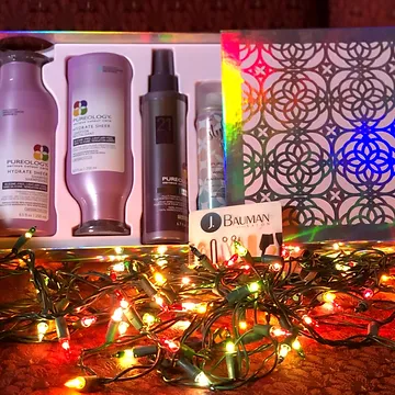 Gift box with various hair care products including shampoo and sprays, decorated with colorful twinkling christmas lights in the foreground.