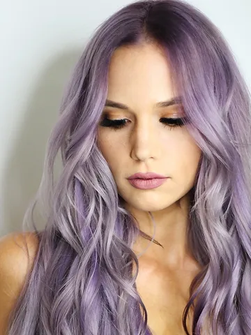 A woman with long, wavy lavender hair looking downwards. she has a subtle makeup look with smokey eyes and nude lipstick.