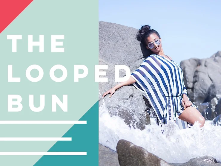 A woman with a looped bun hairstyle, wearing sunglasses and a striped cover-up, sits on a rocky beach as waves splash around her. the image has a graphic overlay with text "the looped bun.