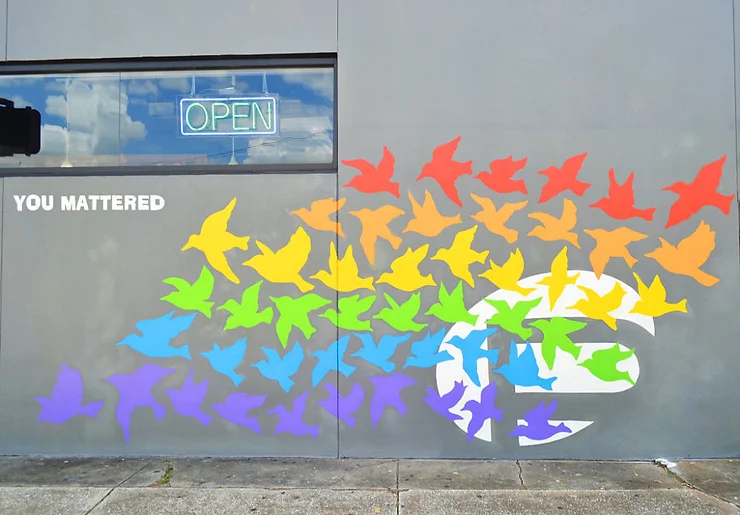 A vibrant mural on a gray wall featuring a swarm of colorful birds in red, orange, yellow, green, blue, and purple. the words "you mattered" are displayed above in white text.