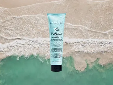 A tube of bumble and bumble don't blow it hair styler placed on the edge where clear ocean water meets sandy beach.