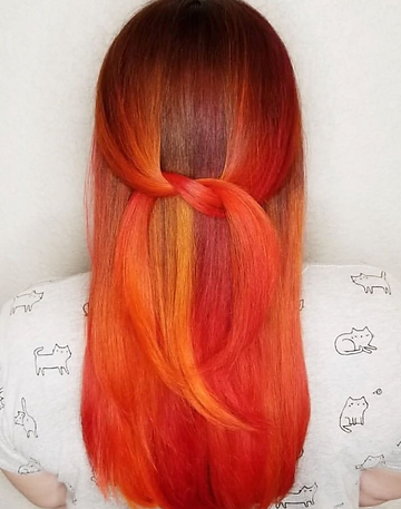 A woman with long hair showcasing a gradient hair color from red at the top to yellow at the ends, styled in a simple knot. she is wearing a shirt with cat patterns.