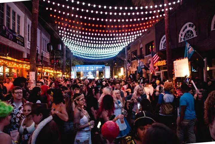 A lively street festival at night with crowds of people in costumes under a canopy of red, white, and blue lights.