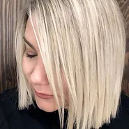 A close-up photo of a woman with a stylish blonde bob haircut, looking down, partially covering her face with her hair.