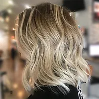 A woman's hairstyle featuring shoulder-length, wavy, blonde hair with darker roots, photographed in a salon setting. the focus is on the hair texture and color.